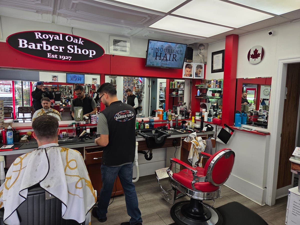 Inside Royal Oak Barber Shop: barbers at work at the red chairs under the shop's oval sign